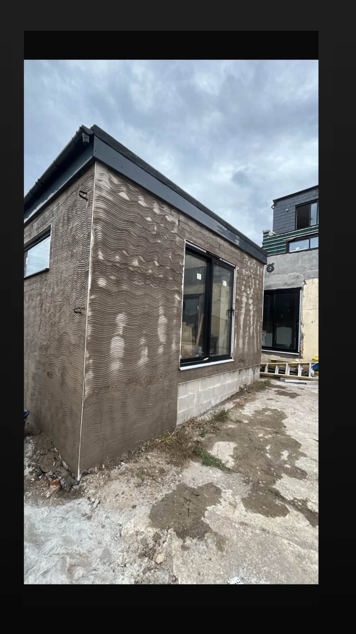 Exterior of an extension with installed black-framed glazing and unfinished render