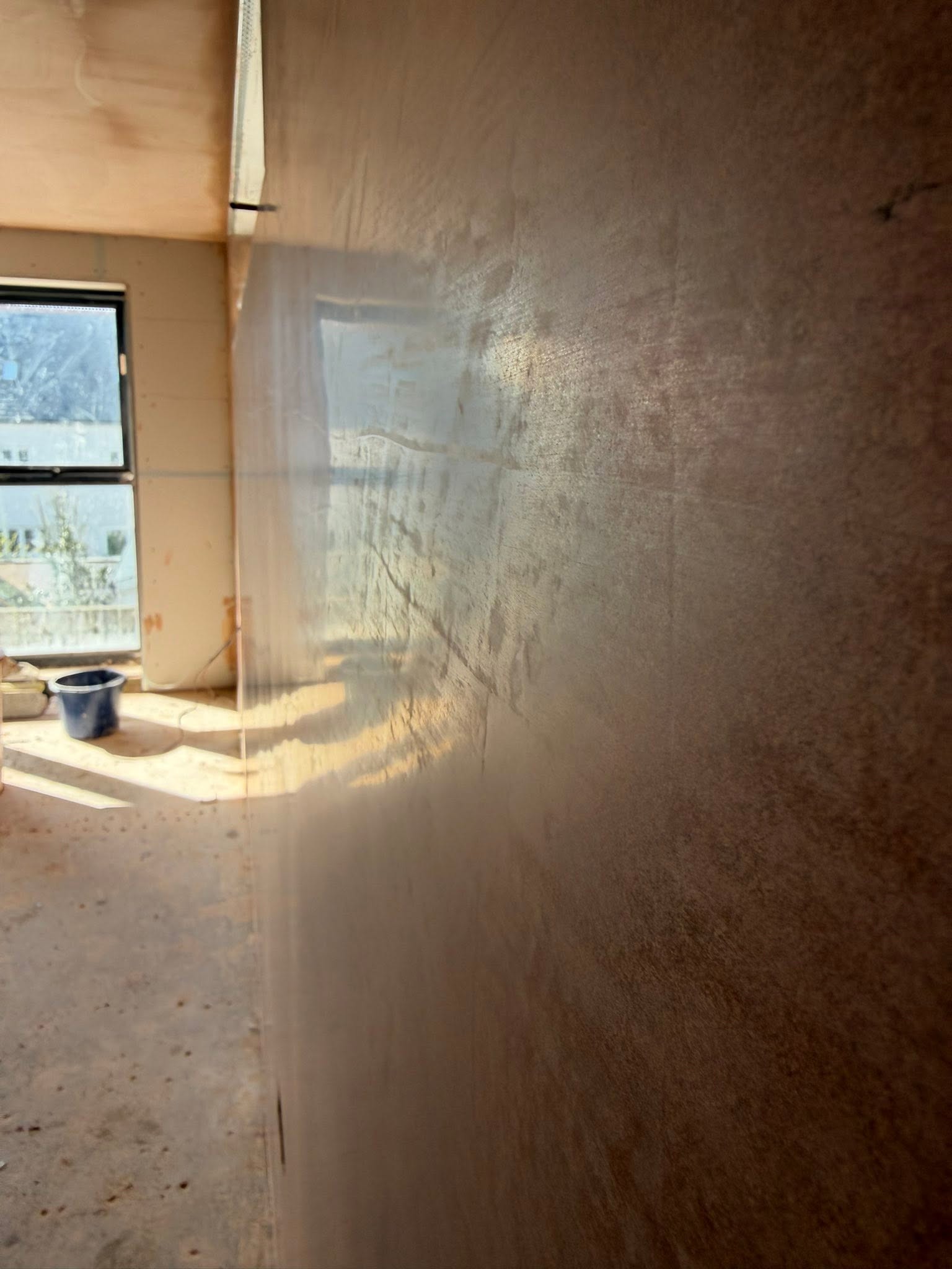 Daylight and a window reflected across a glossy orange-brown plaster wall