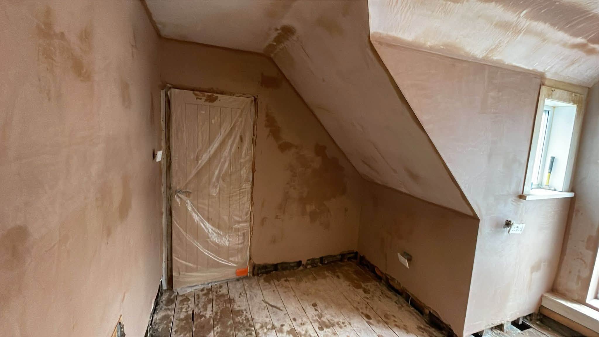 Freshly plastered room with a sloping ceiling and exposed floorboards