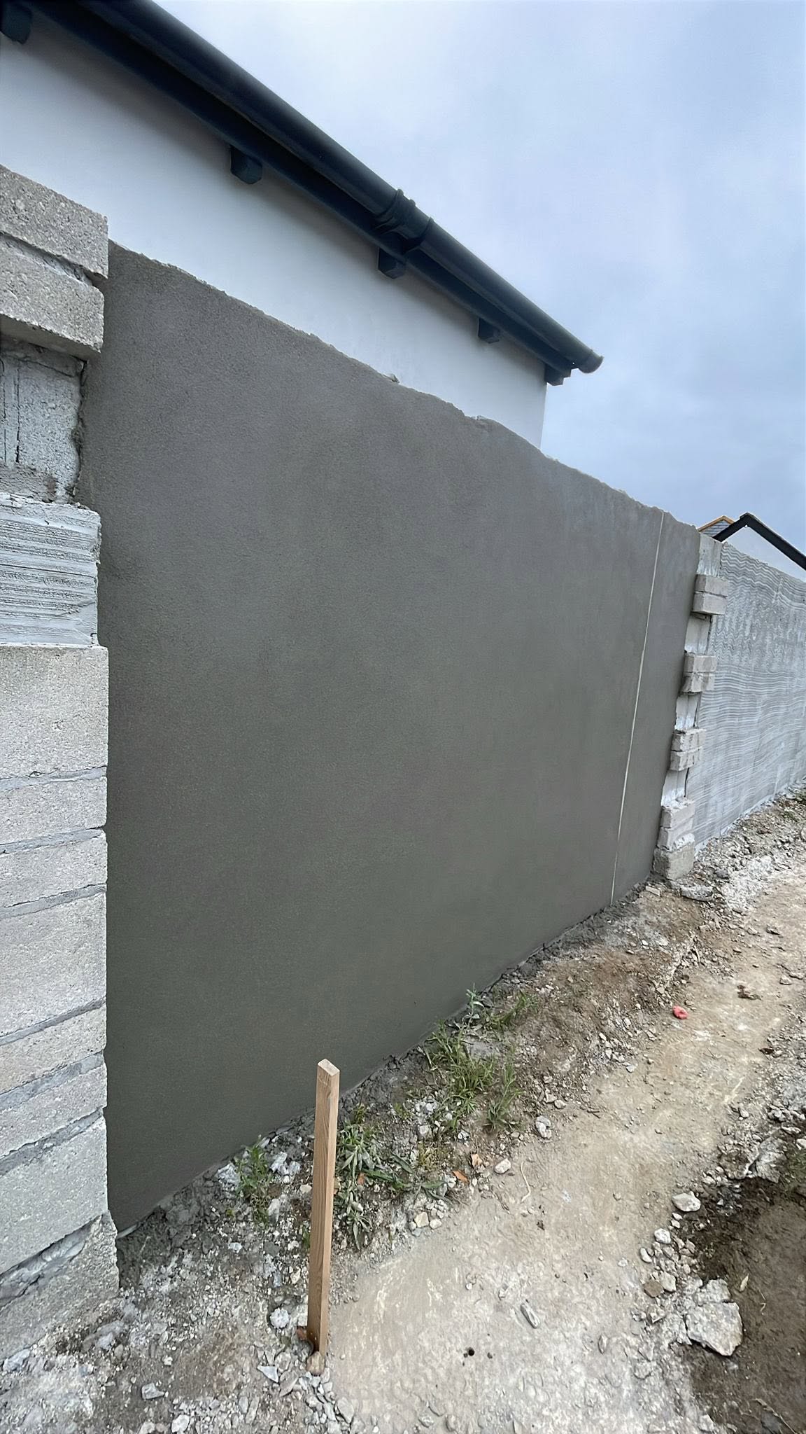 The same boundary wall with a smooth grey top coat between the block piers