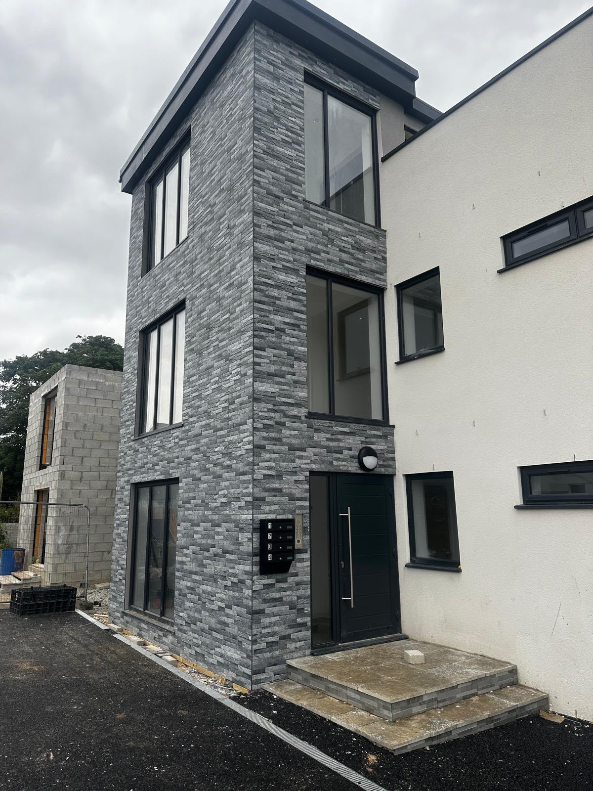 Grey stone cladding around a three-storey entrance and black-framed windows, beside white render