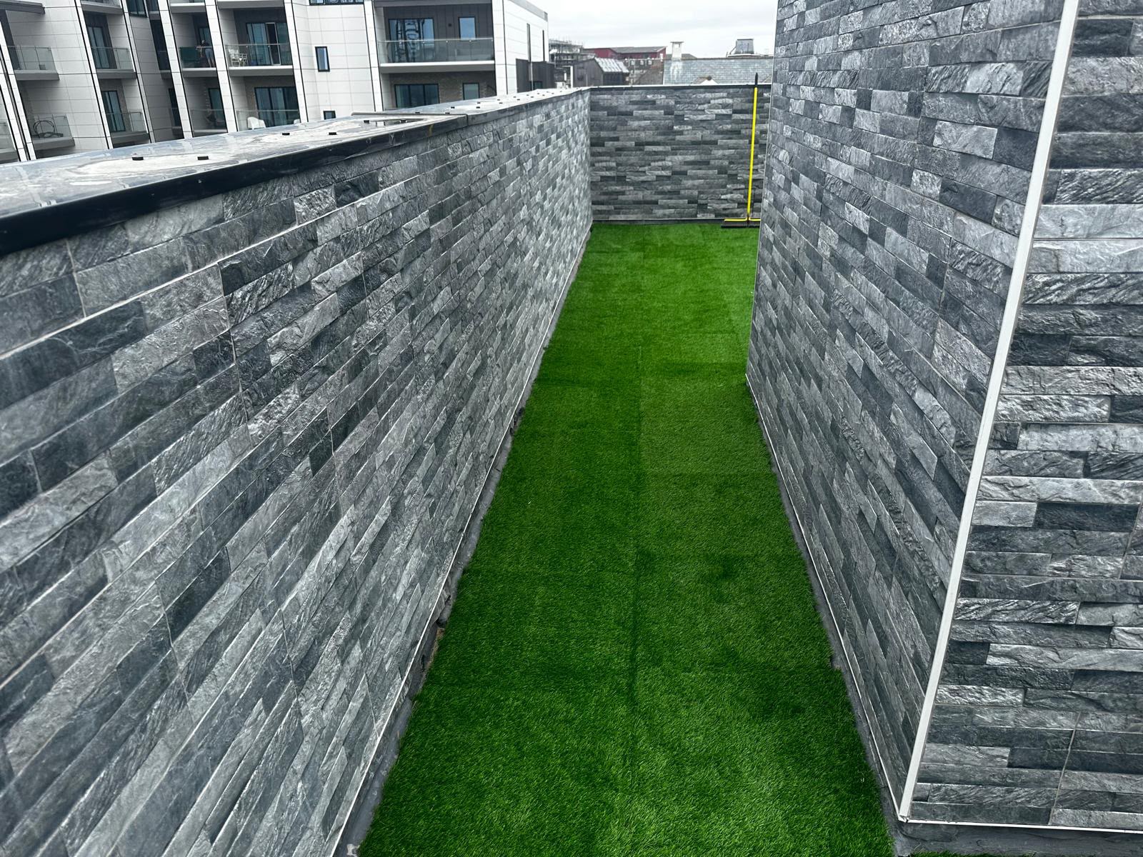 Grey stone-clad terrace walls and corner details alongside green artificial grass