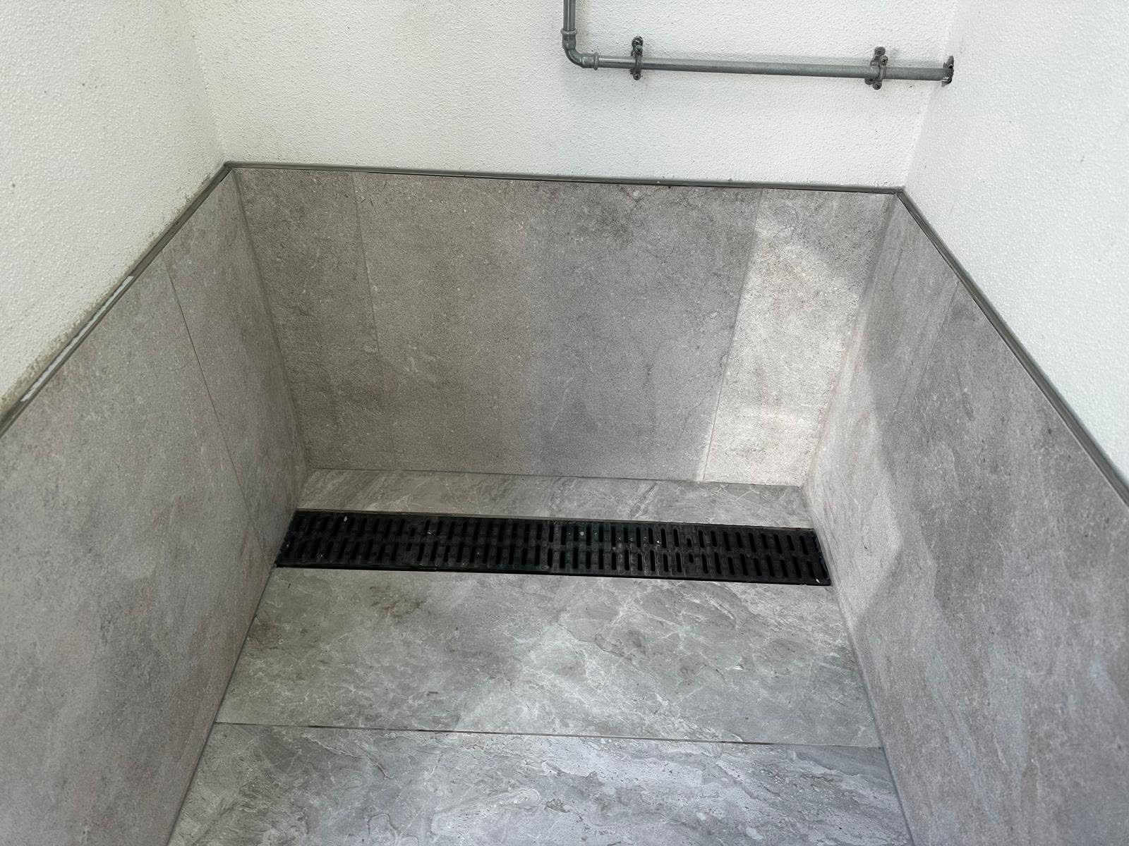 Grey stone-effect tiles meeting a black linear shower drain