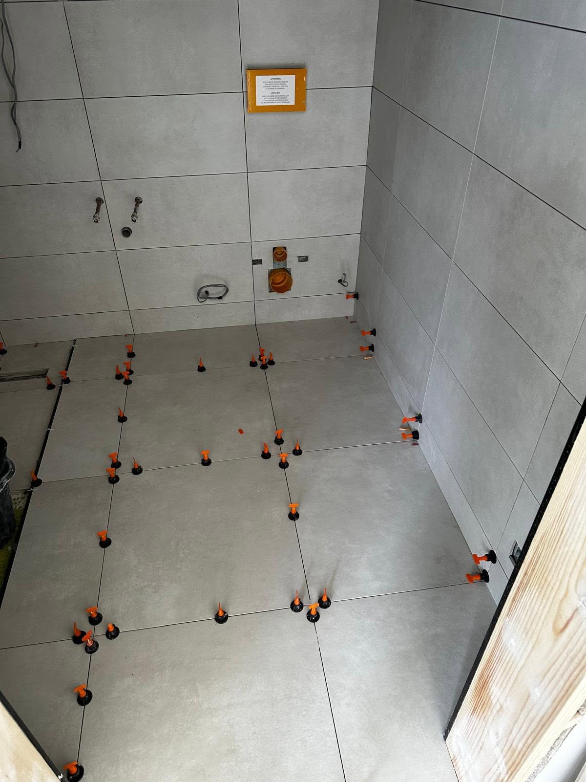 Large wall and floor tiles with orange levelling clips during installation