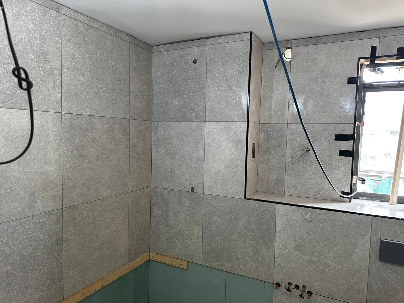 Large grey tiles fitted around a shower niche and window, with fittings still in progress
